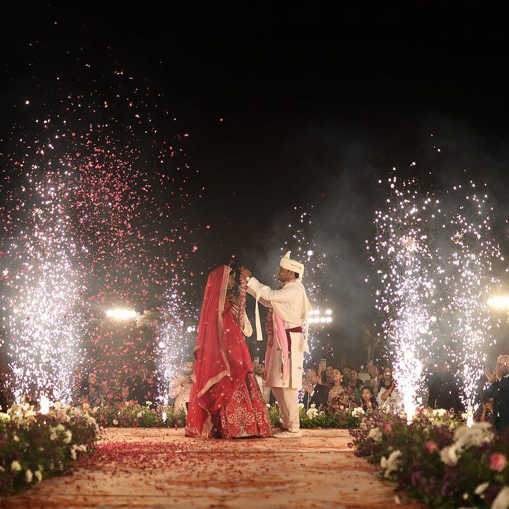 Bride and groom exchanging garlands under a fireworks display